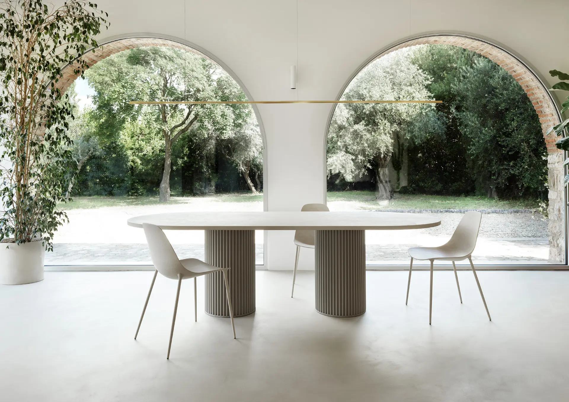 Round table on a fluted base and white chairs beneath two arches opening onto olive trees