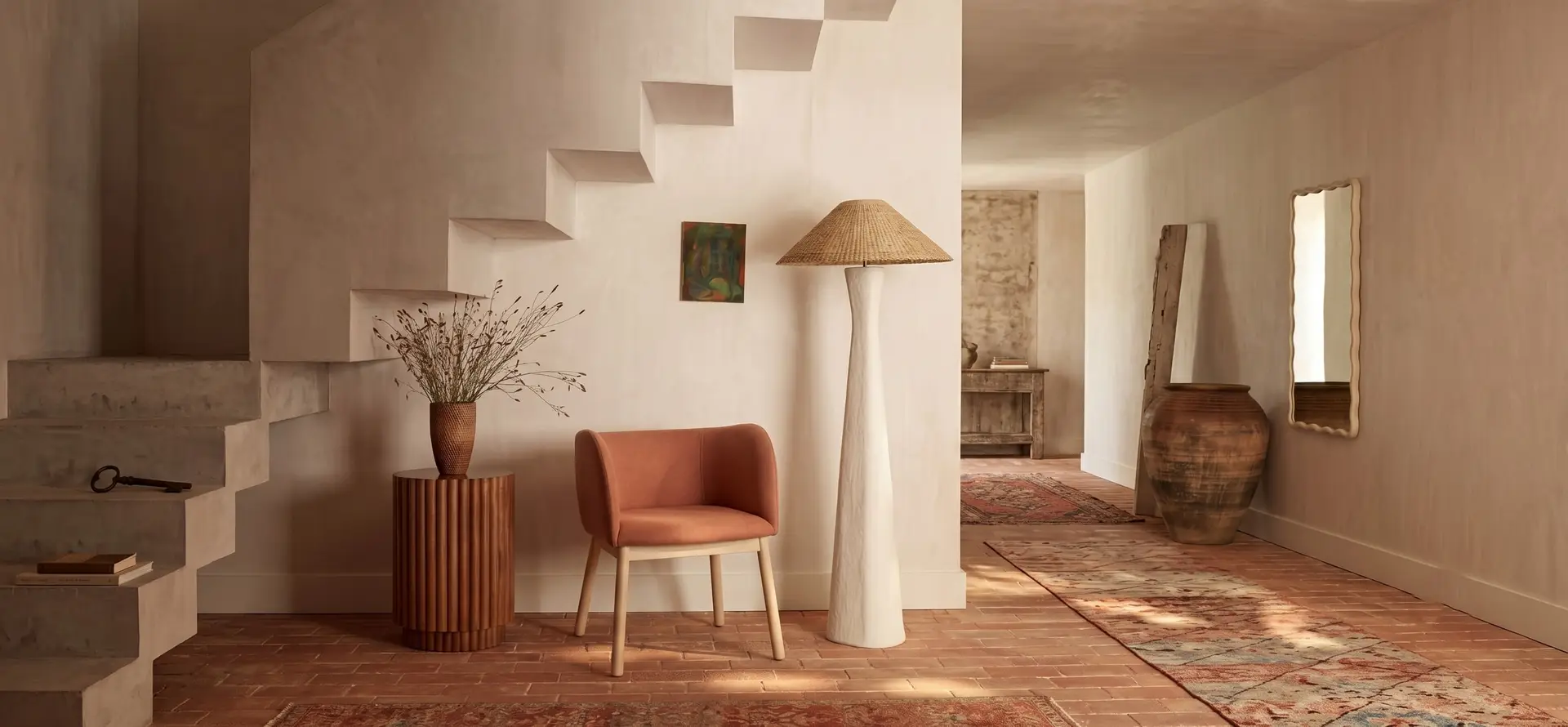 Terracotta armchair and a round side table beneath a white plaster stair
