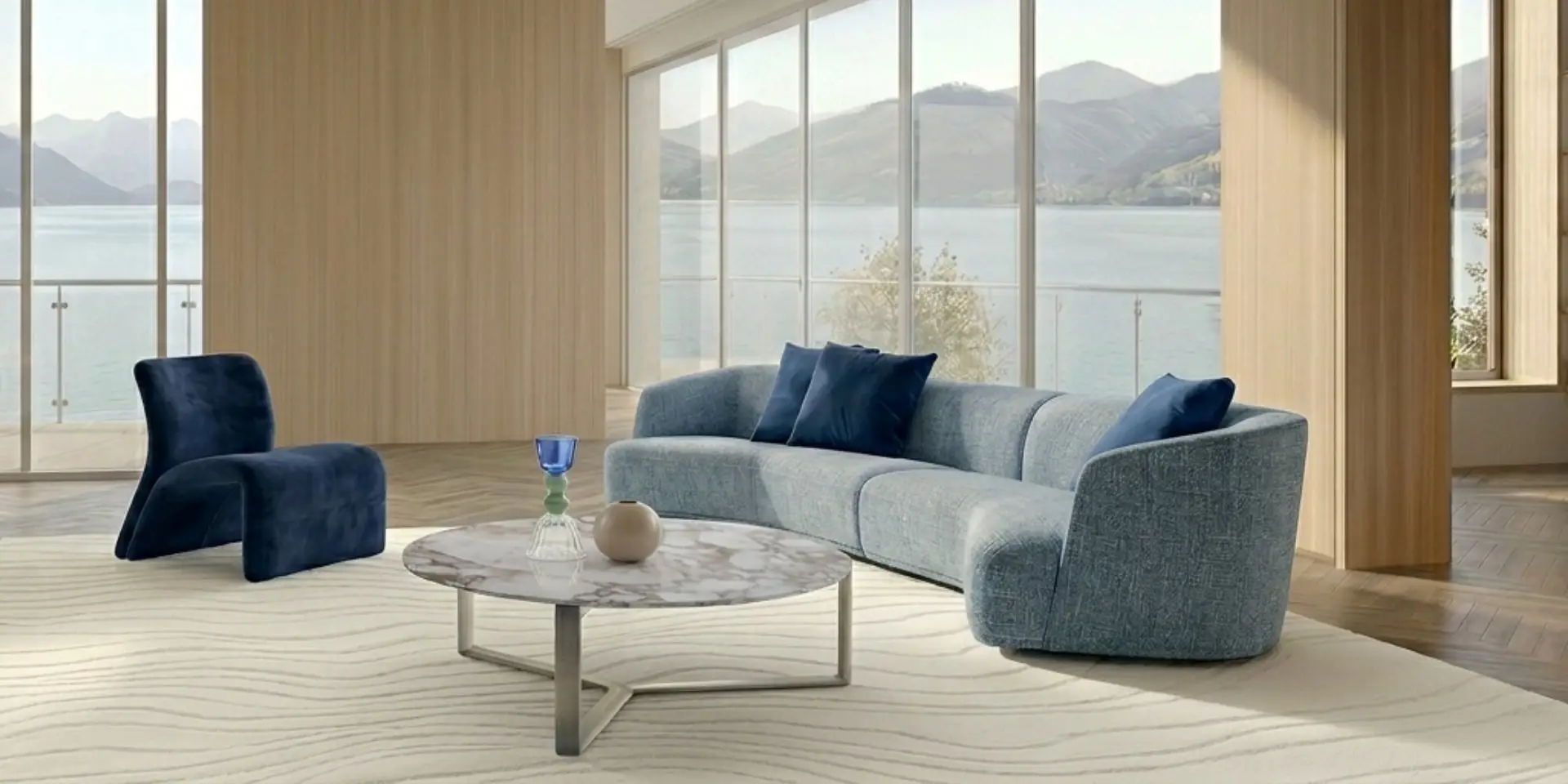 Curved blue sofa and armchair around a marble coffee table in a room facing a lake