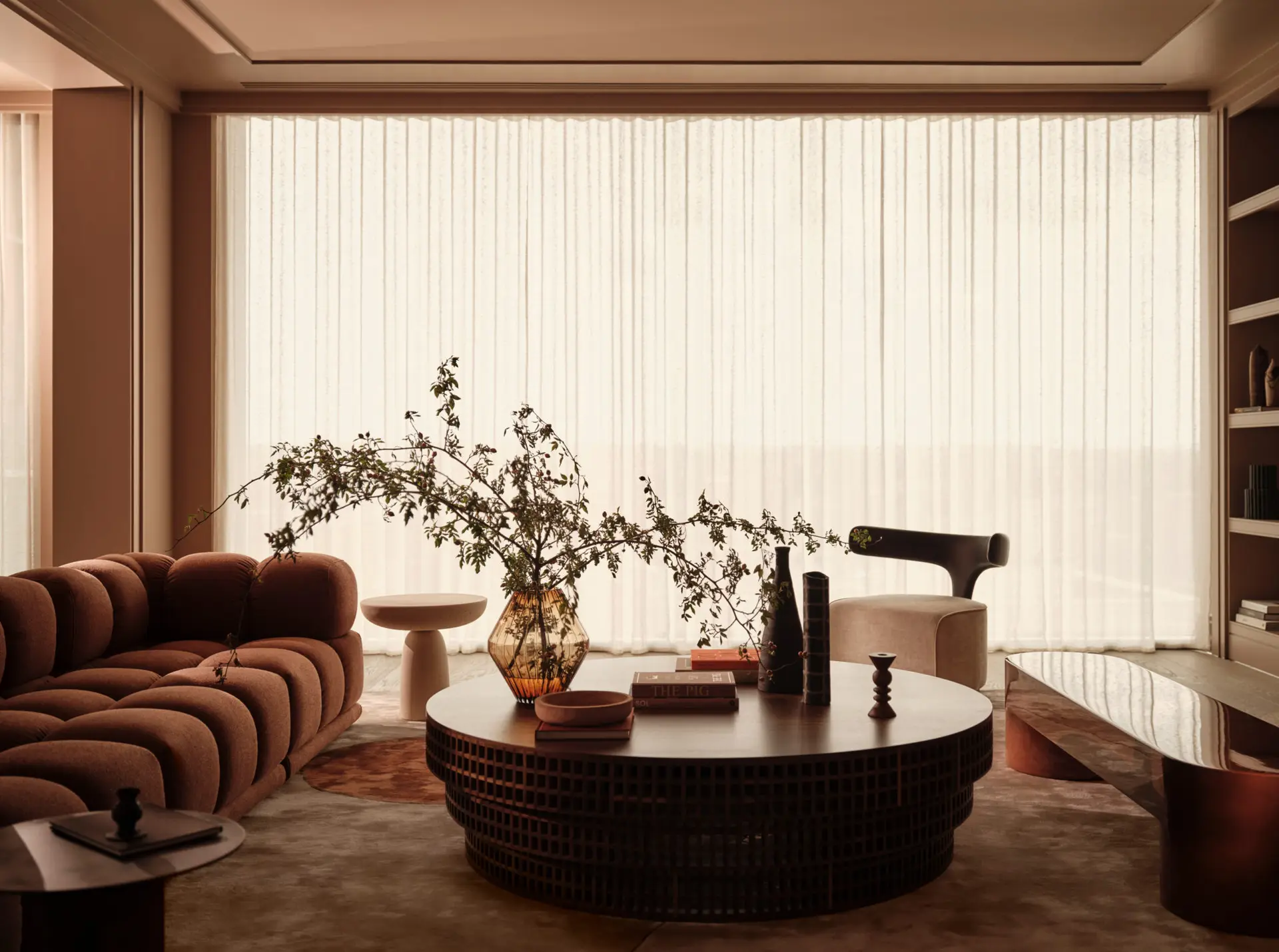 Rust channel-quilted sofa and a round dark coffee table in a warm room with sheer curtains