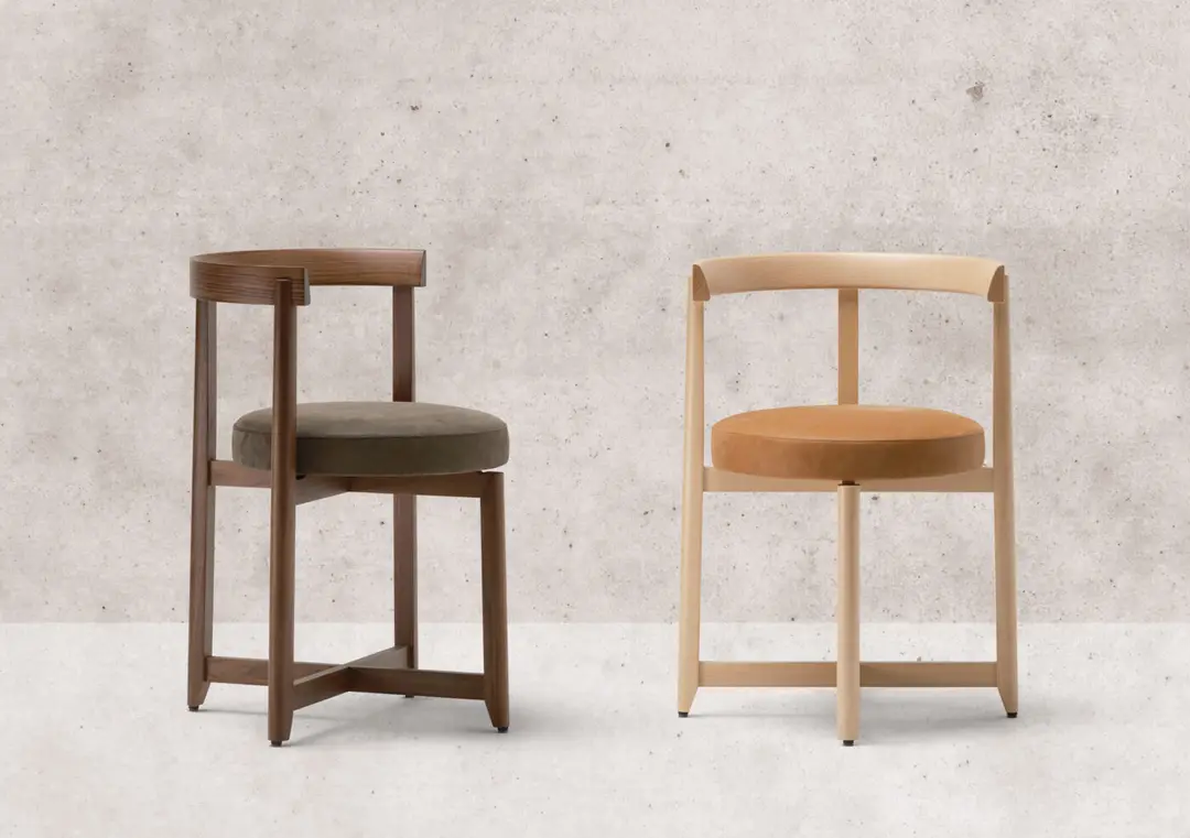 Two wooden chairs with round upholstered seats against a concrete wall