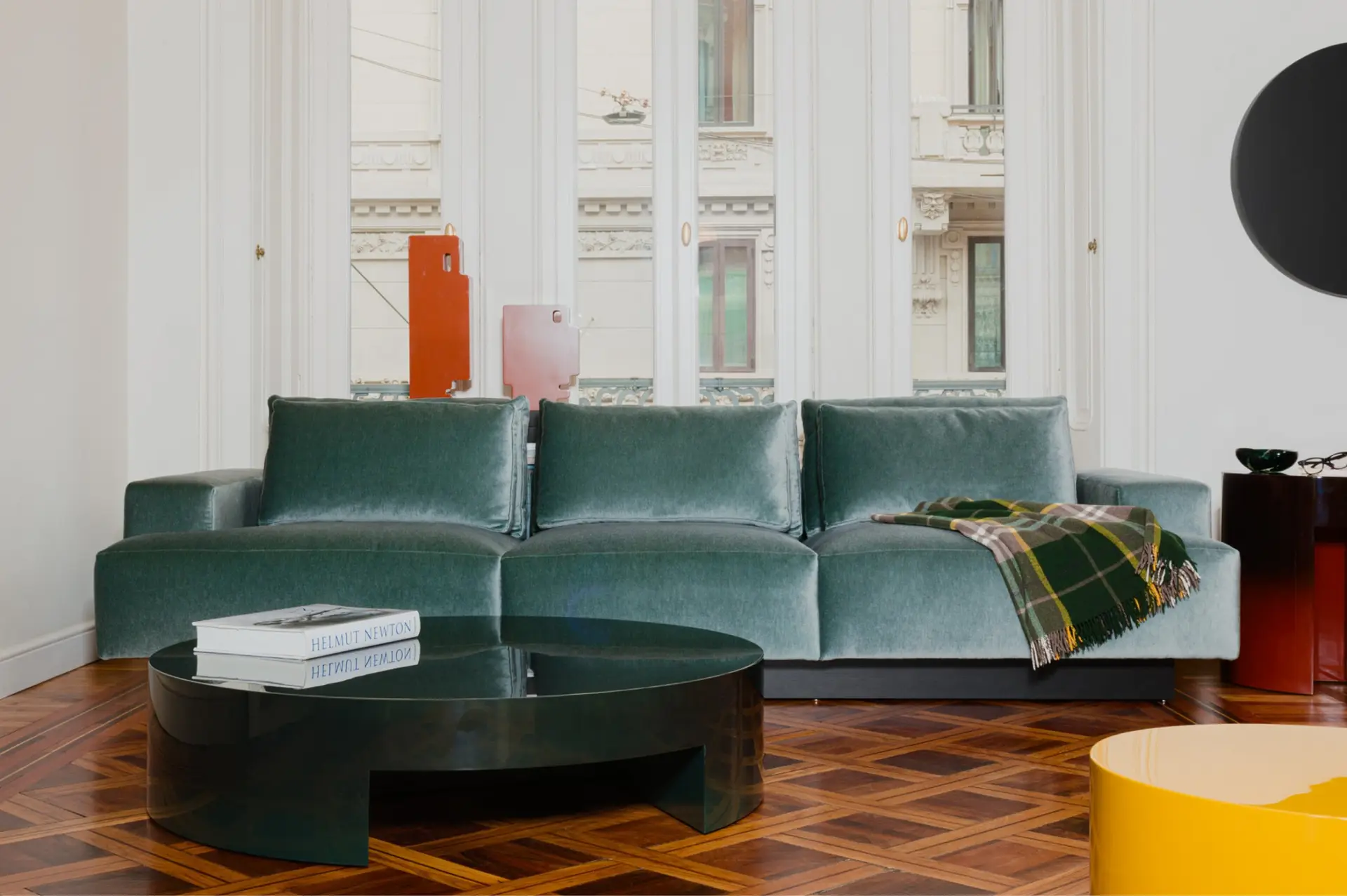 Teal velvet sofa and a round black coffee table on a patterned parquet floor