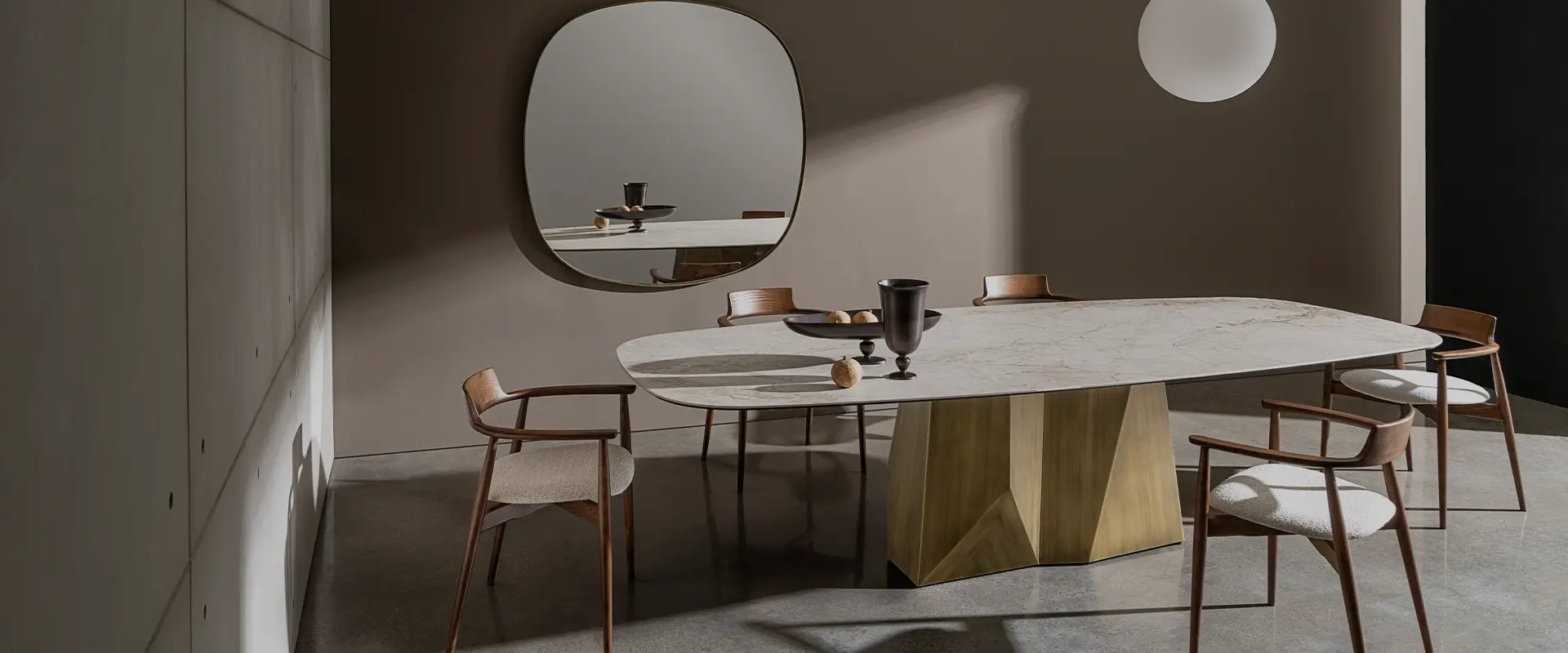 Oval dining table on a faceted timber base beneath a soft-cornered mirror and a globe lamp