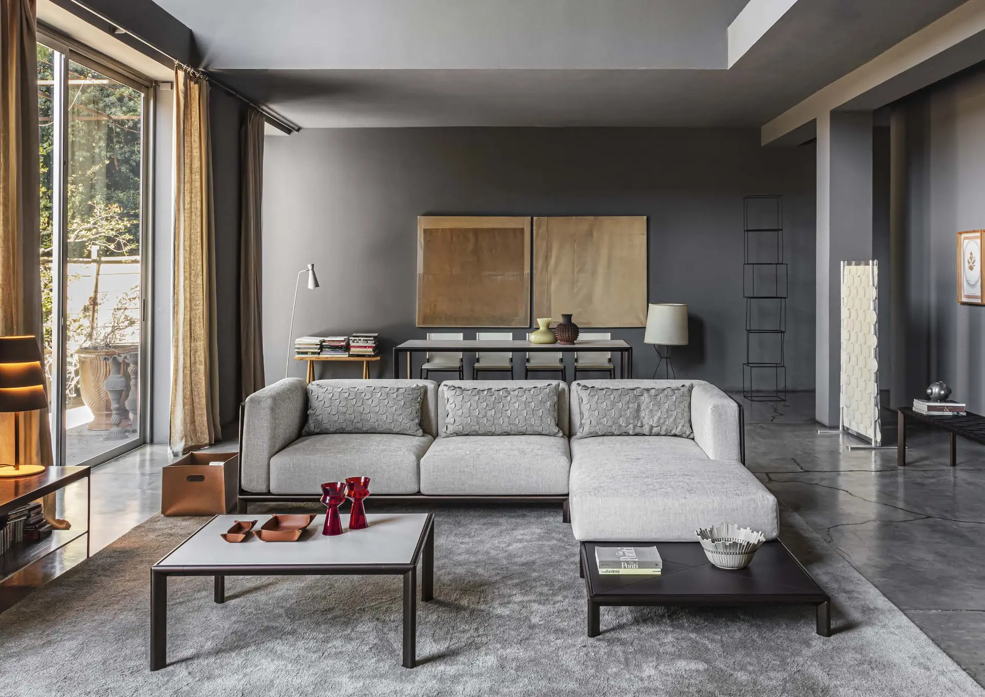 Pale corner sofa and leather-framed coffee tables in a grey loft with a dining table behind