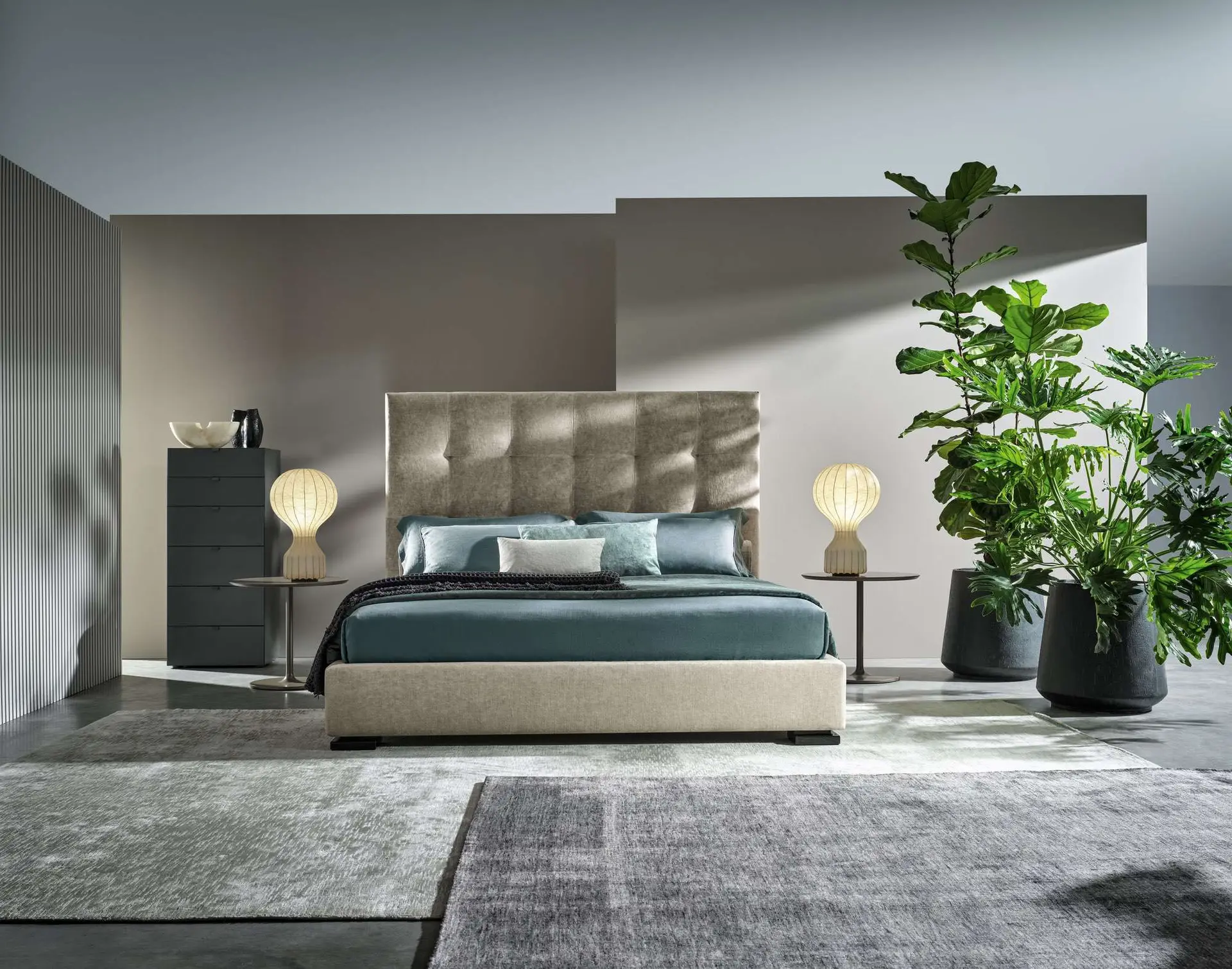 Bed with a tall quilted headboard and teal bedding between globe lamps and large plants