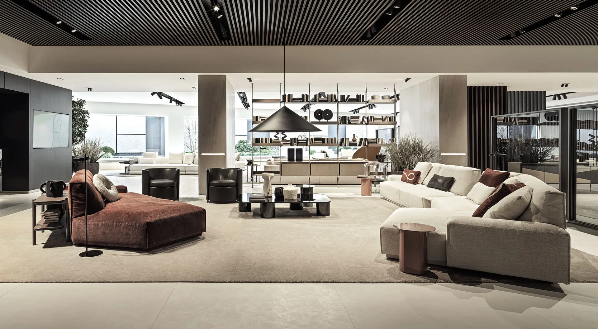 Showroom living area with low sofas, a burgundy daybed and tall shelving under a slatted ceiling