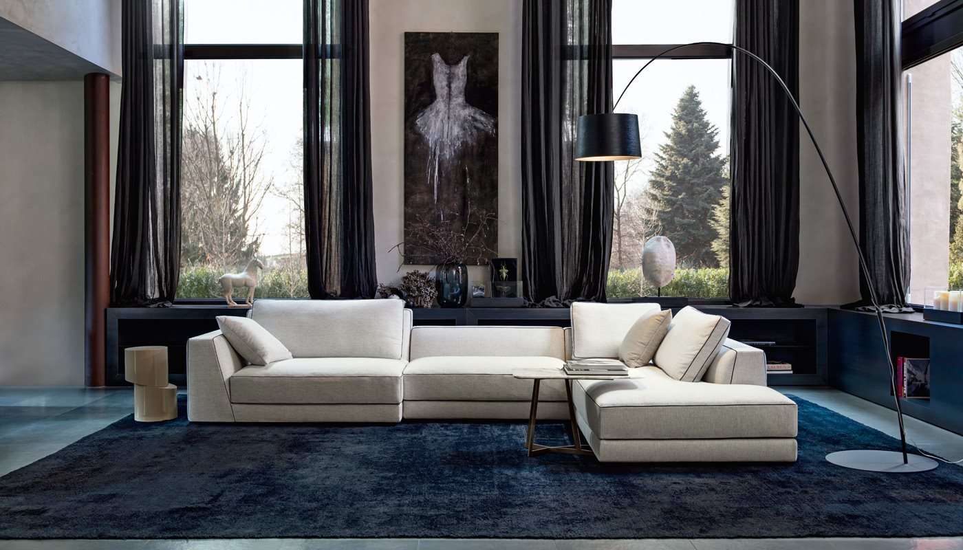 Cream corner sofa on a dark blue rug before tall windows and dark curtains