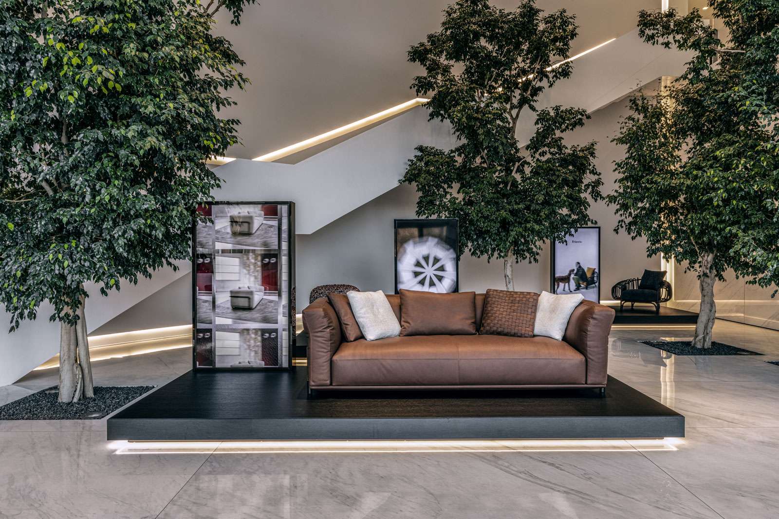 Tan leather sofa on a black plinth among indoor trees