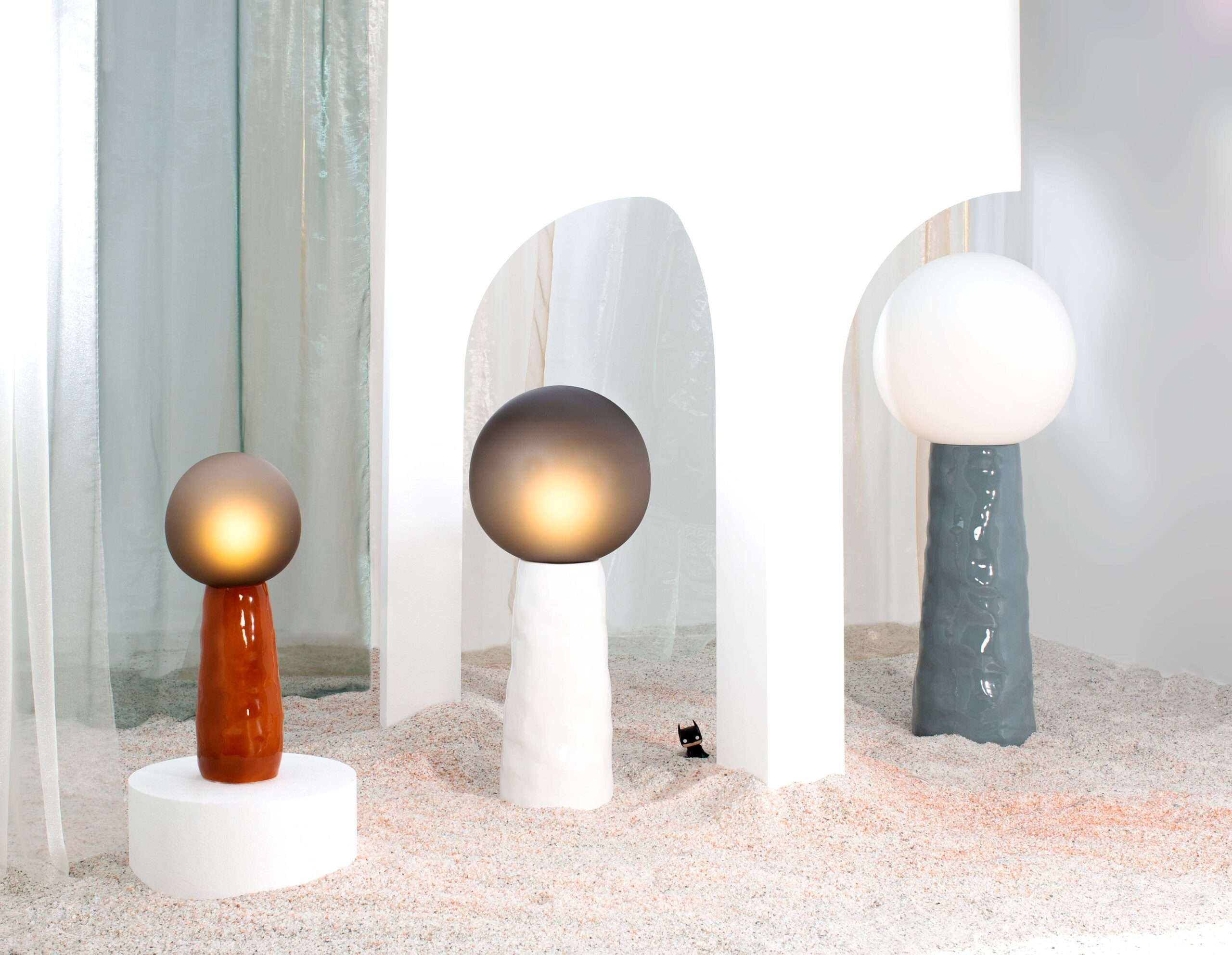 Table lamps with glowing glass globes standing on sand between white arches