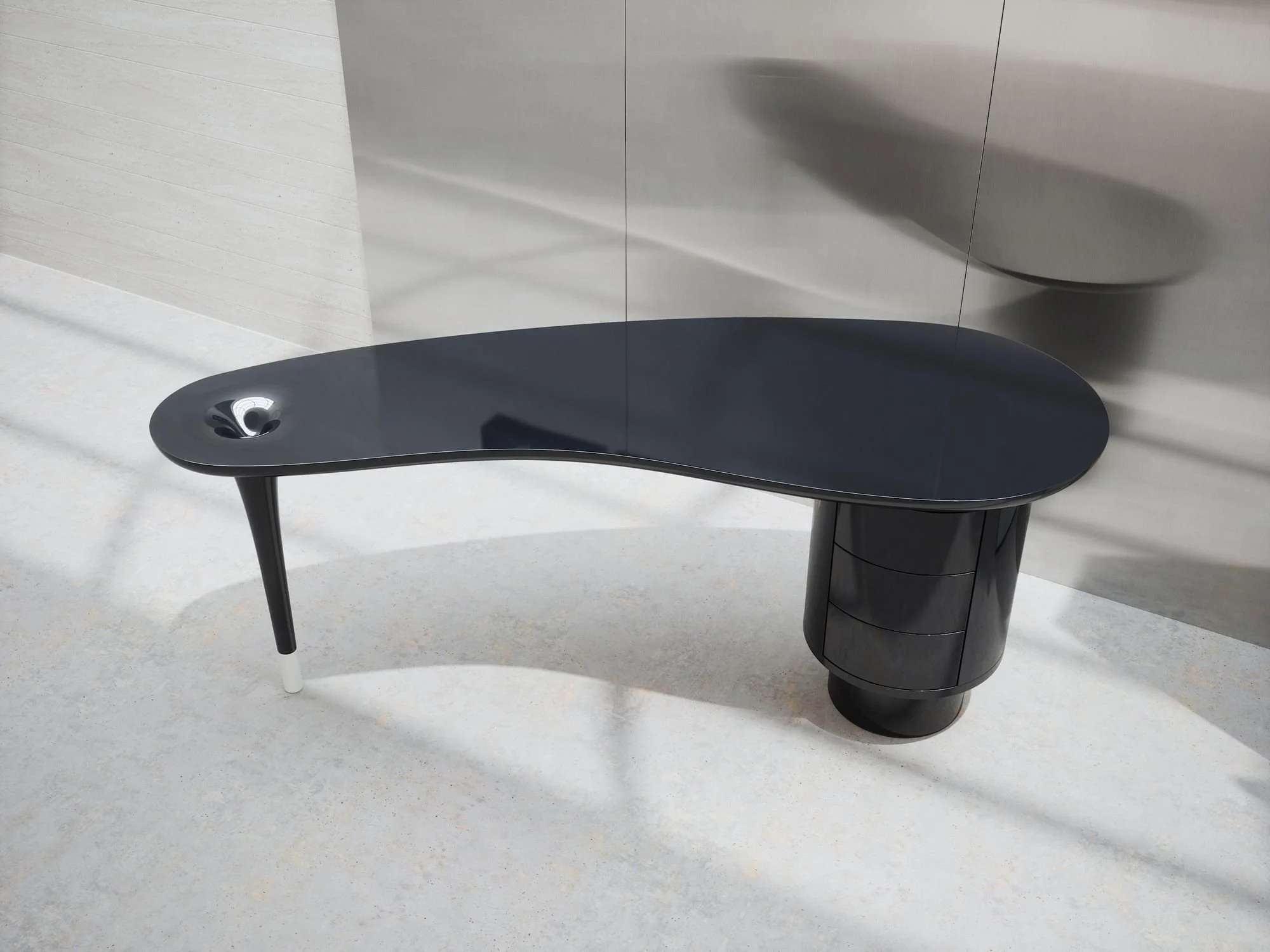 Black desk with a curved top on a sculpted leg, in soft daylight