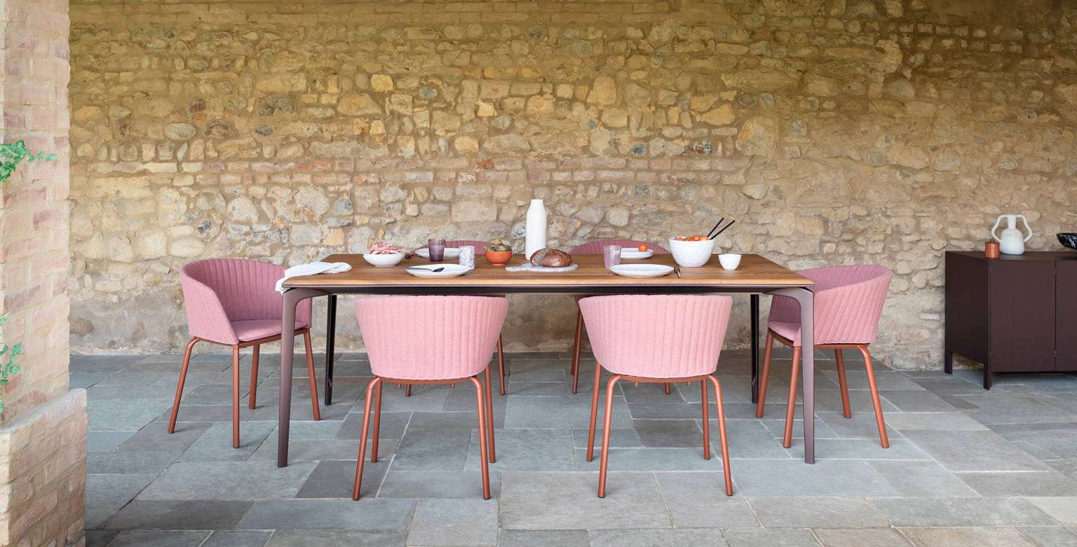 Pink outdoor chairs around a long table against a rough stone wall