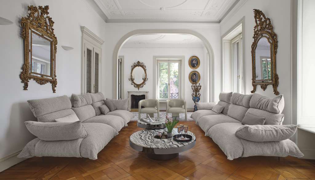 Pale grey sofas around a low table in a classical room with gilded mirrors