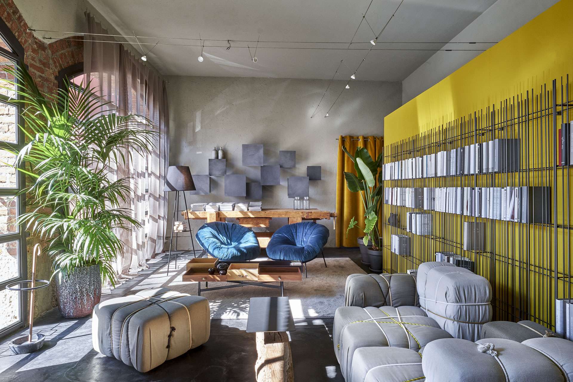 Grey modular sofas and blue armchairs before a yellow wall of wire bookshelves