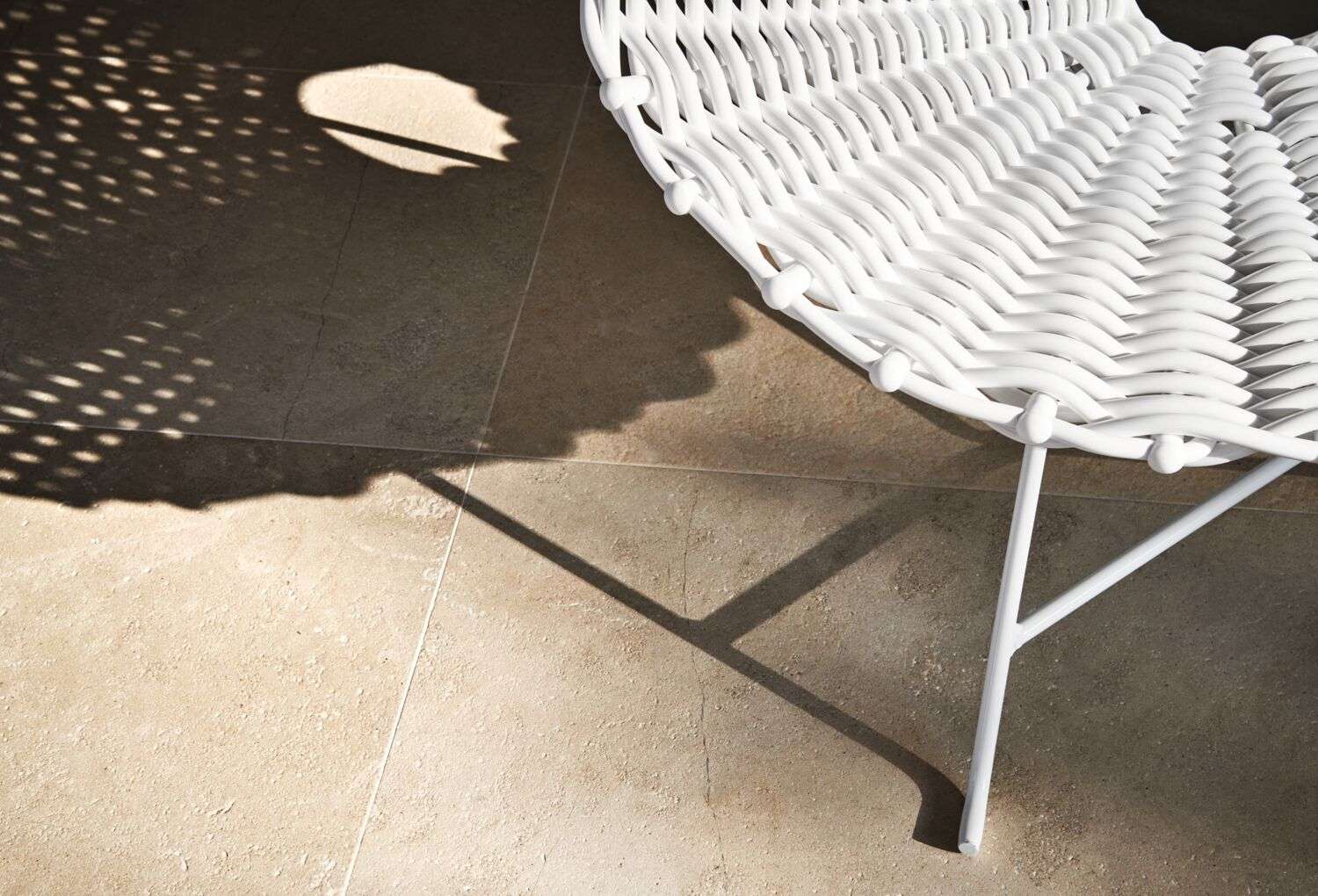 Close-up of a white woven chair casting a patterned shadow on stone