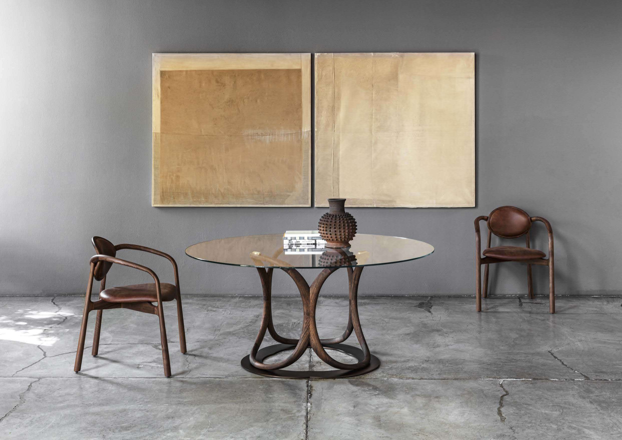 Round glass table on a curving walnut base between two leather-seated armchairs