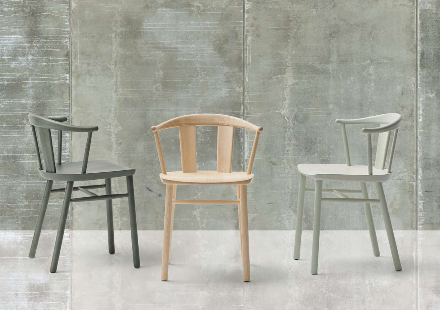 Three spindle-back wooden chairs in grey, natural and pale finishes against concrete