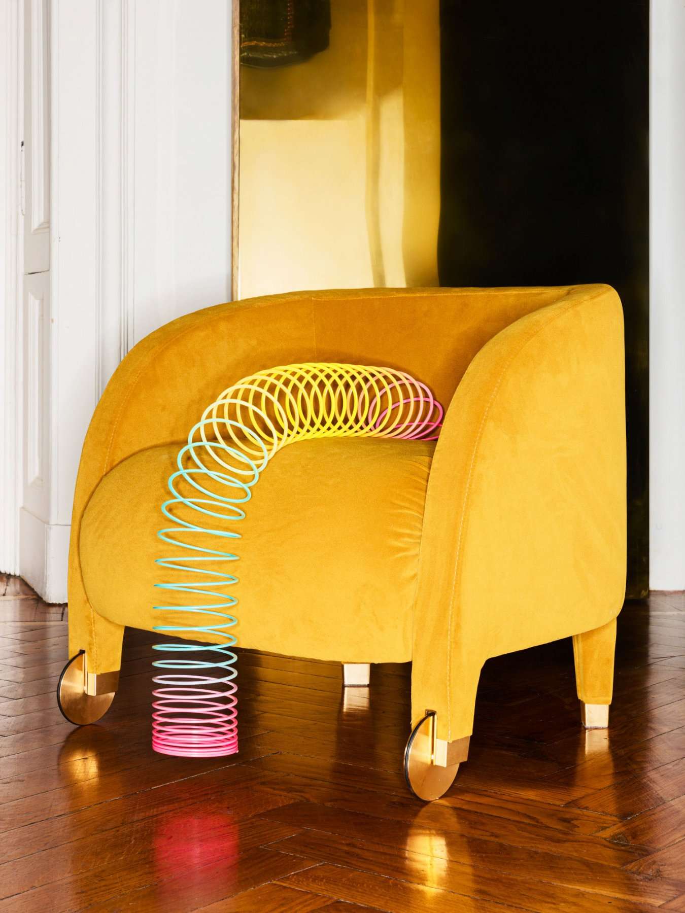 Mustard velvet armchair with a rainbow spring toy on its arm