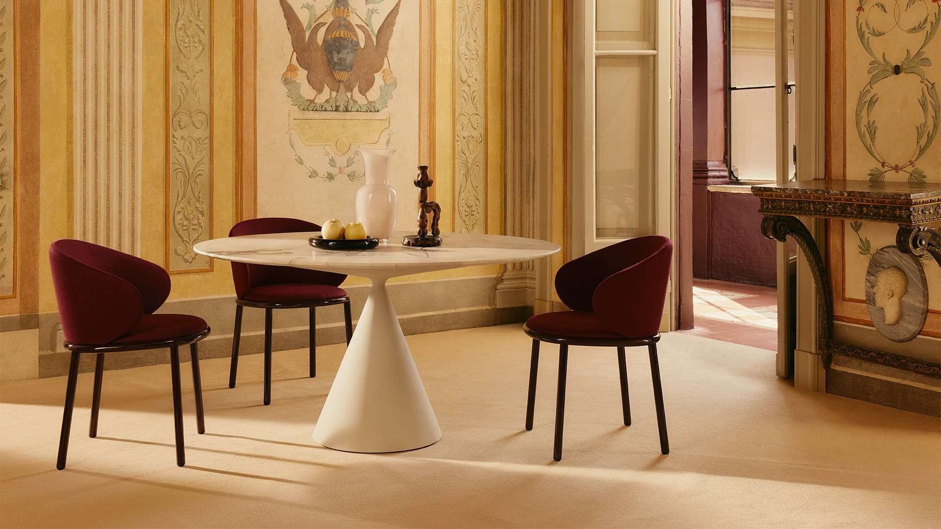 Round white table on a cone base with burgundy chairs in a painted salon