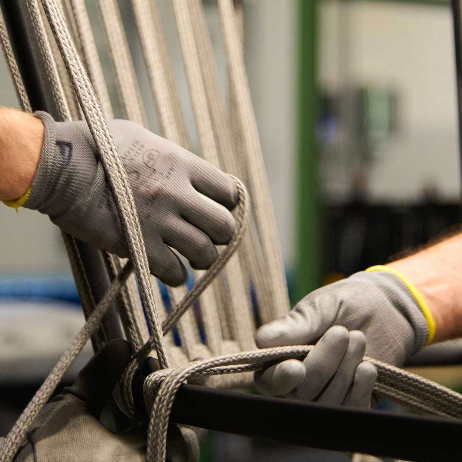 Gloved hands weaving cord onto an aluminium chair frame