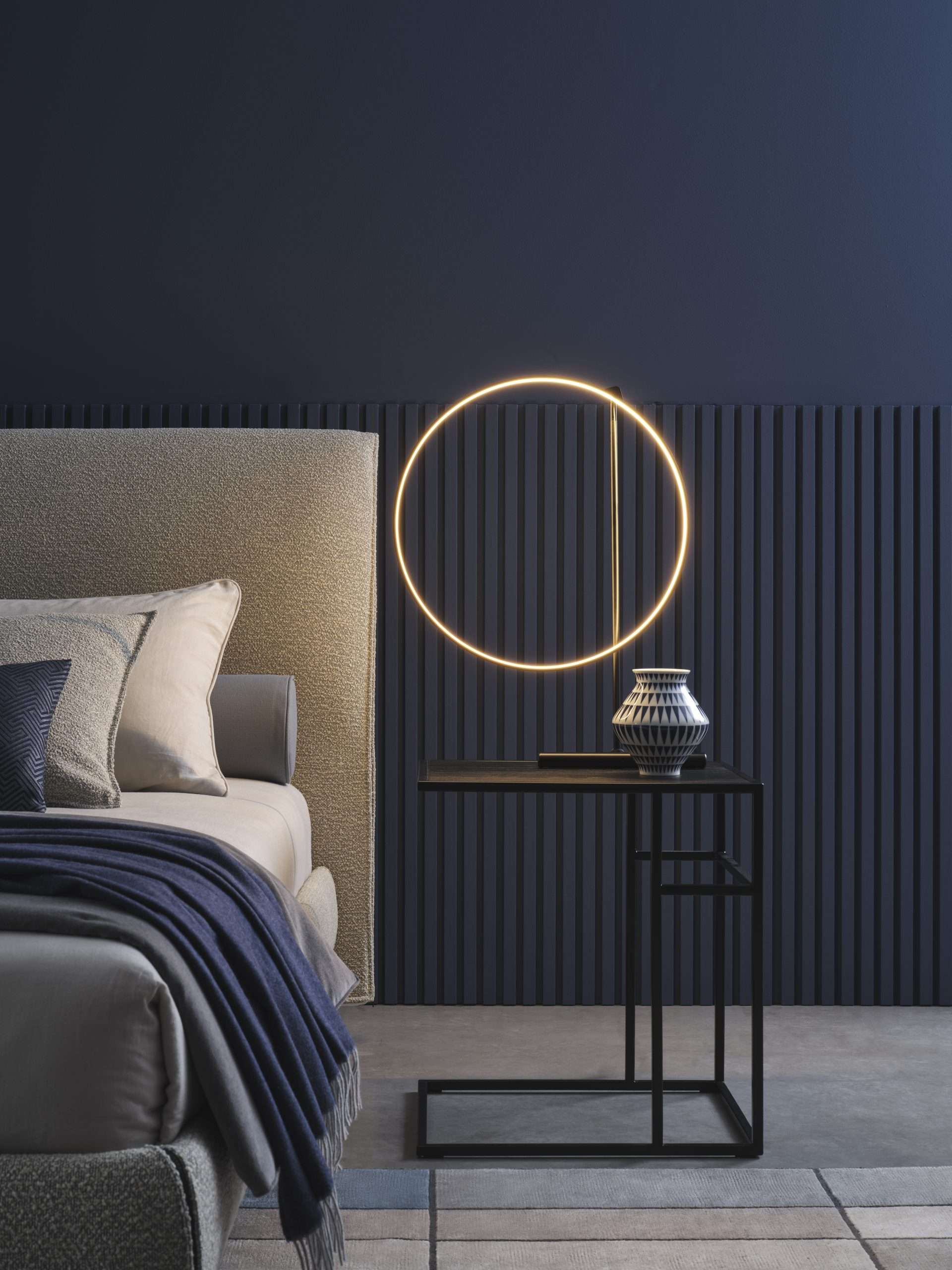 Headboard in sand fabric beside a ring of light on a navy wall