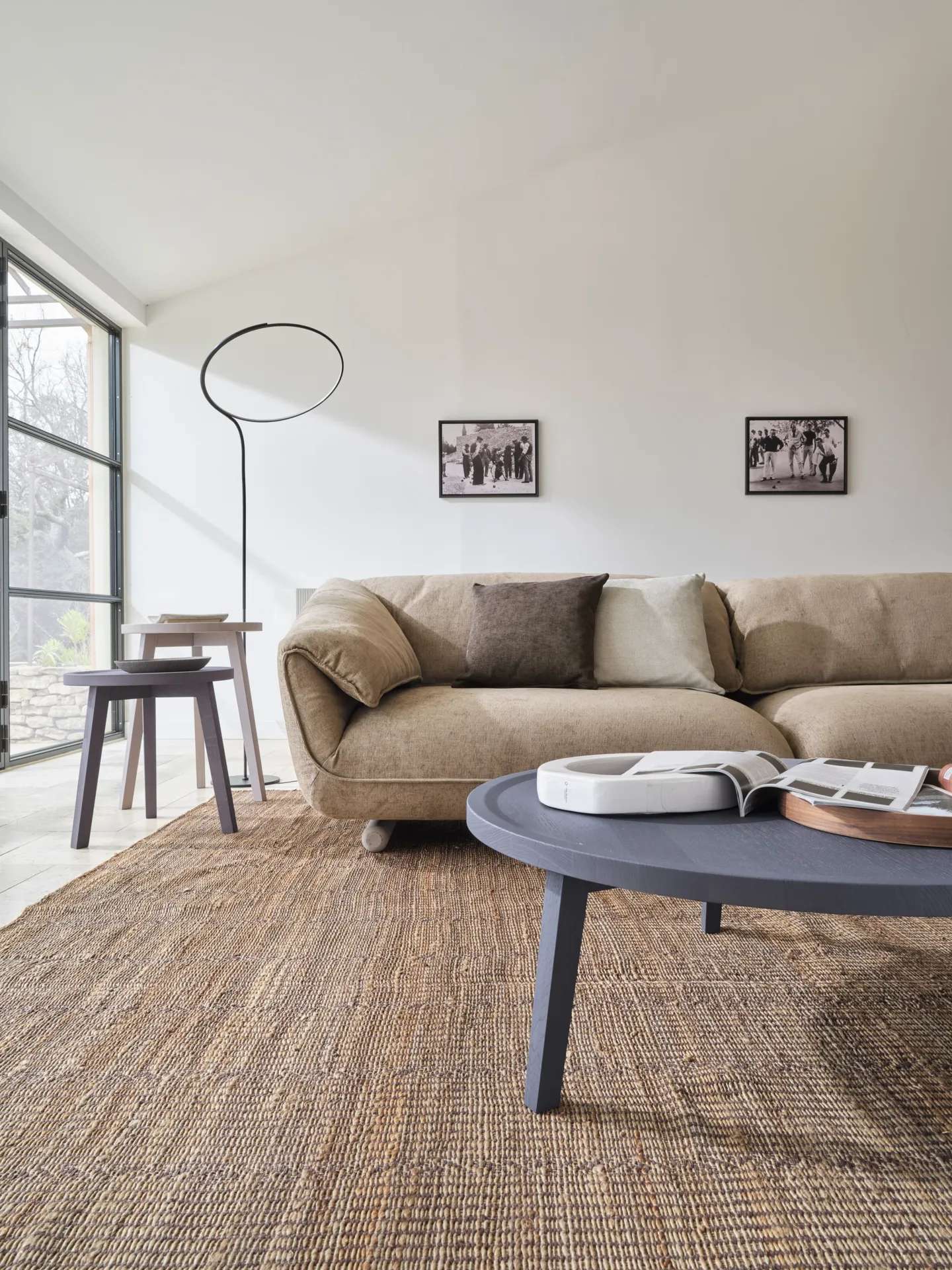 Tan sofa with grey side tables and a round floor lamp in a bright living room