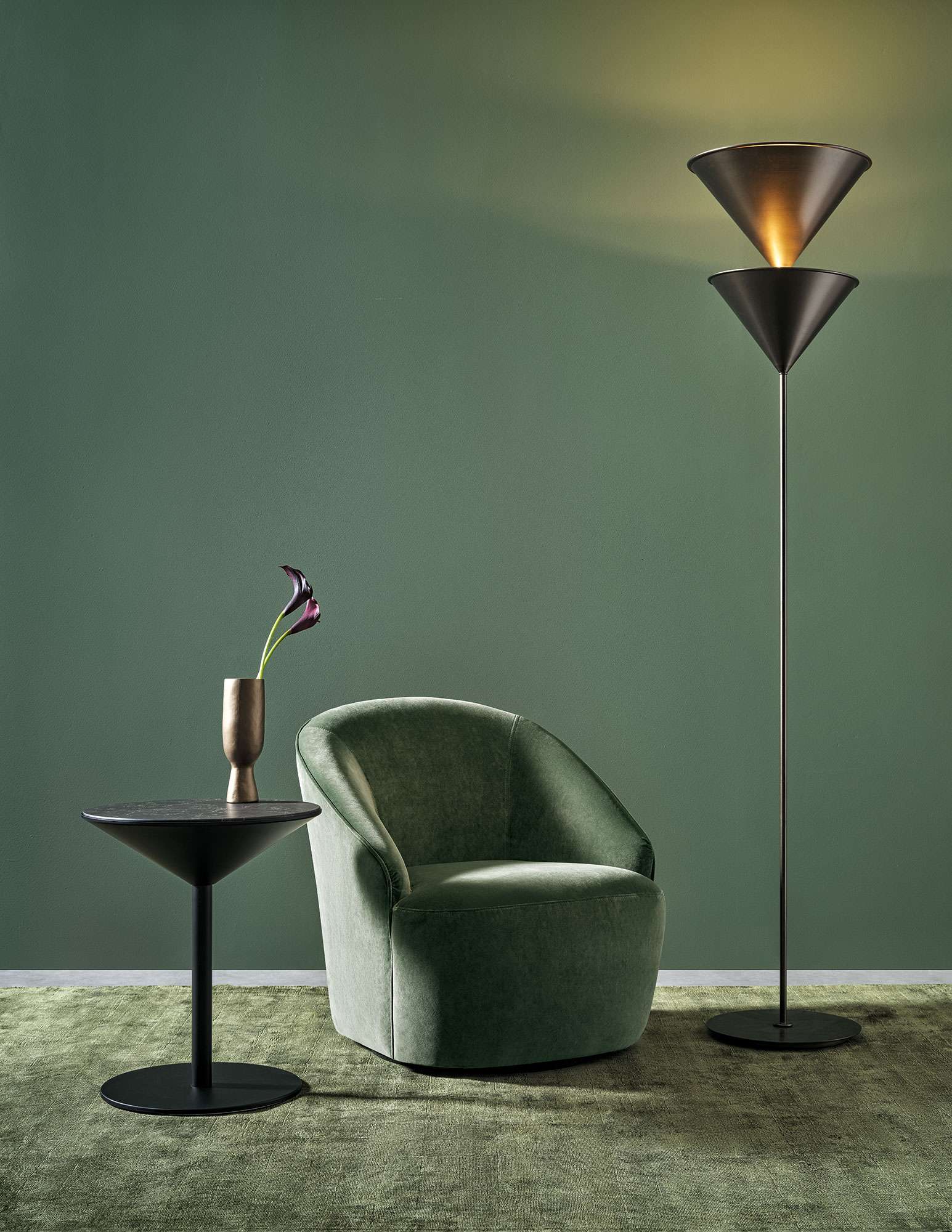 Green velvet armchair against a green wall with a single flower