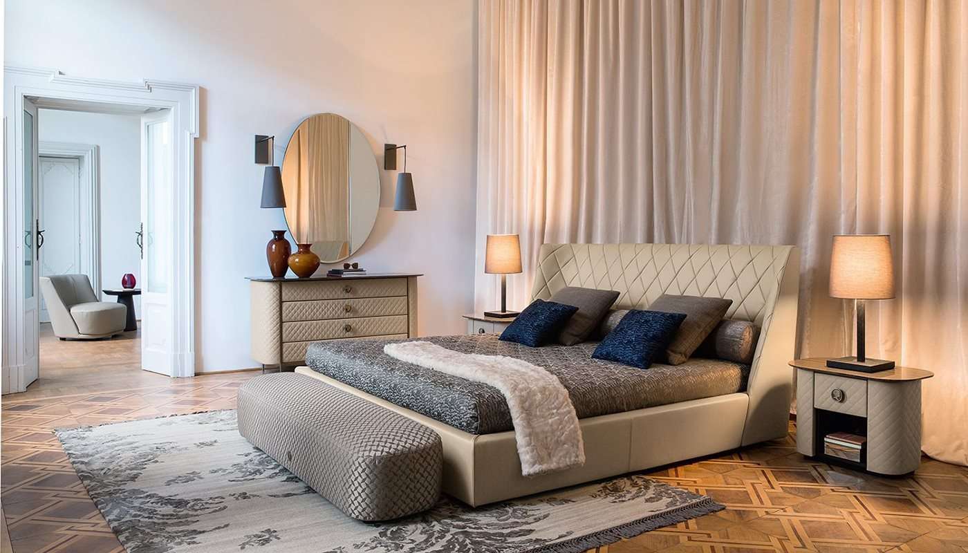 Bed with a quilted leather headboard between bedside lamps and a round mirror