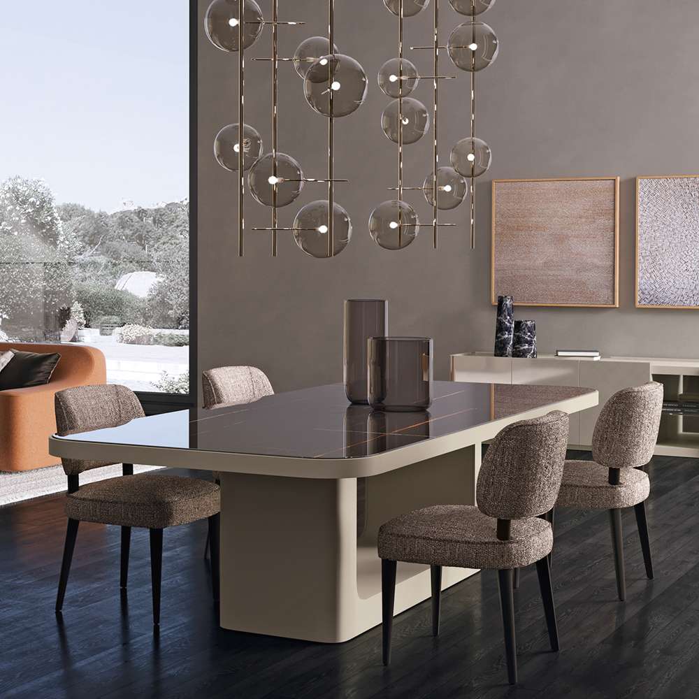 Dining table on a curved pale base with fabric chairs under a cluster of glass globe lights