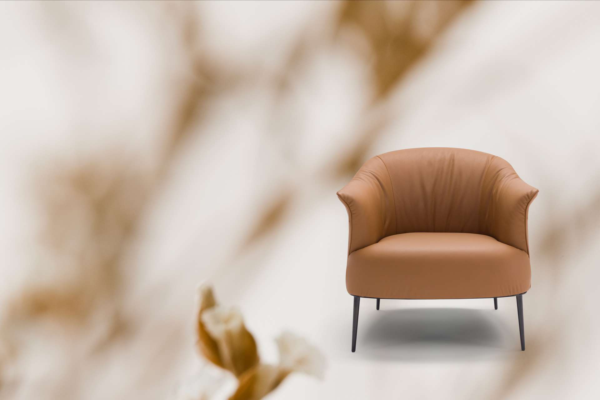Tan leather armchair with a curved back and slim black legs
