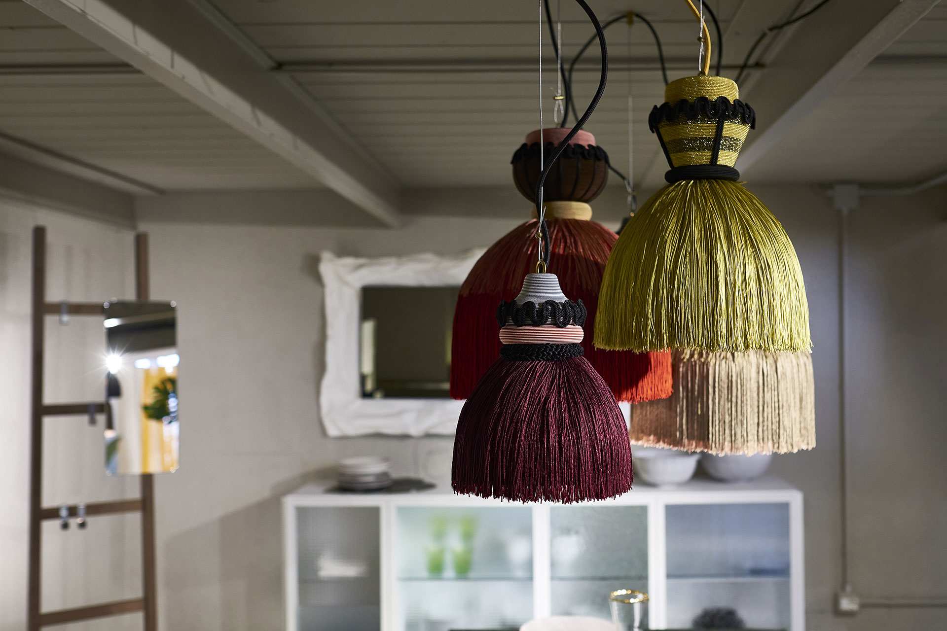 Fringed pendant lamps in burgundy and straw before a white baroque mirror, a leaning ladder and a white cabinet