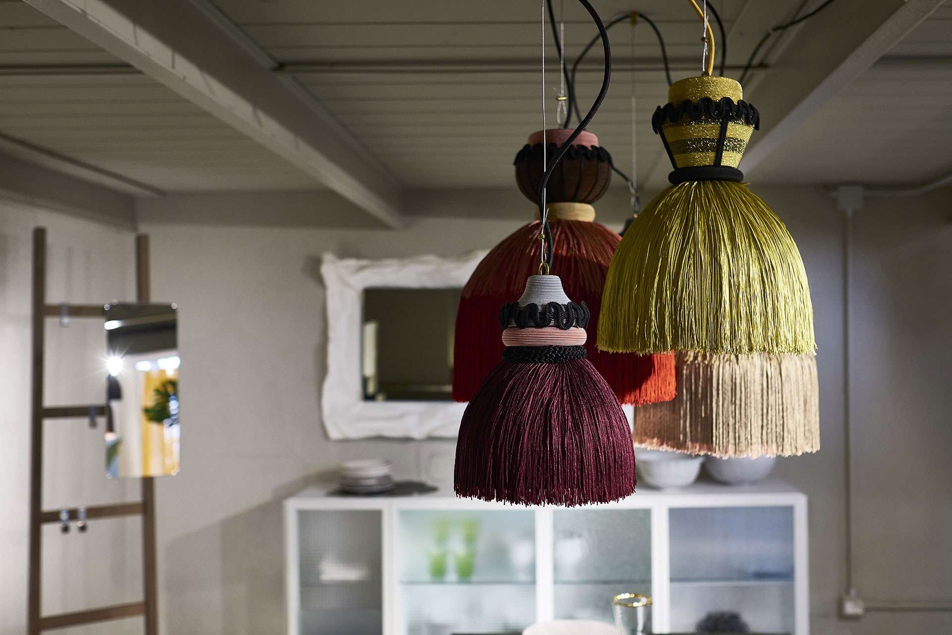 Fringed pendant lamps in burgundy and straw hanging over a white cabinet