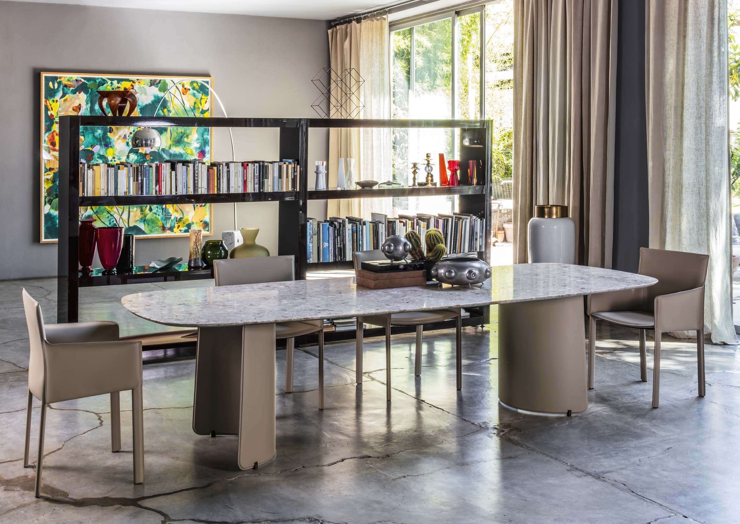 Oval stone dining table on leather-clad bases with leather armchairs before a bookcase