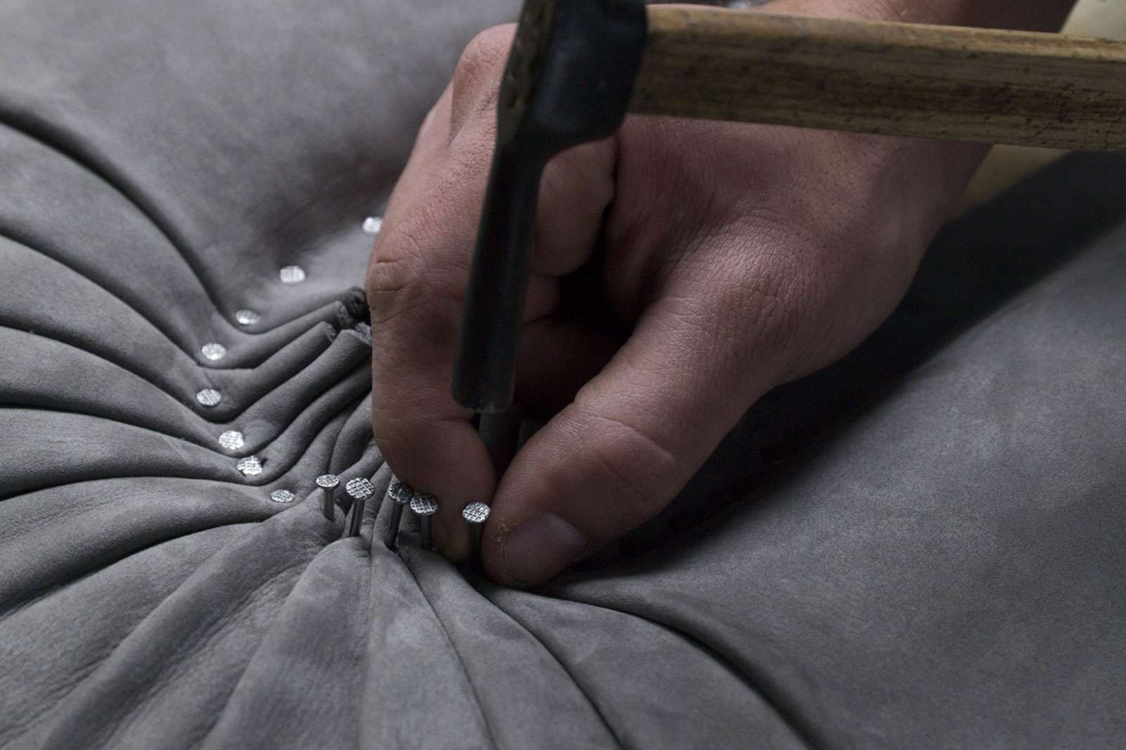 A craftsman pleating upholstery fabric with a tufting tool