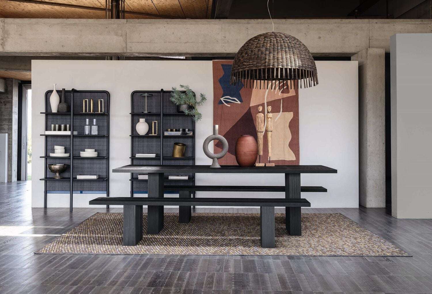 Long dark dining table and benches under a woven pendant, with black shelving behind