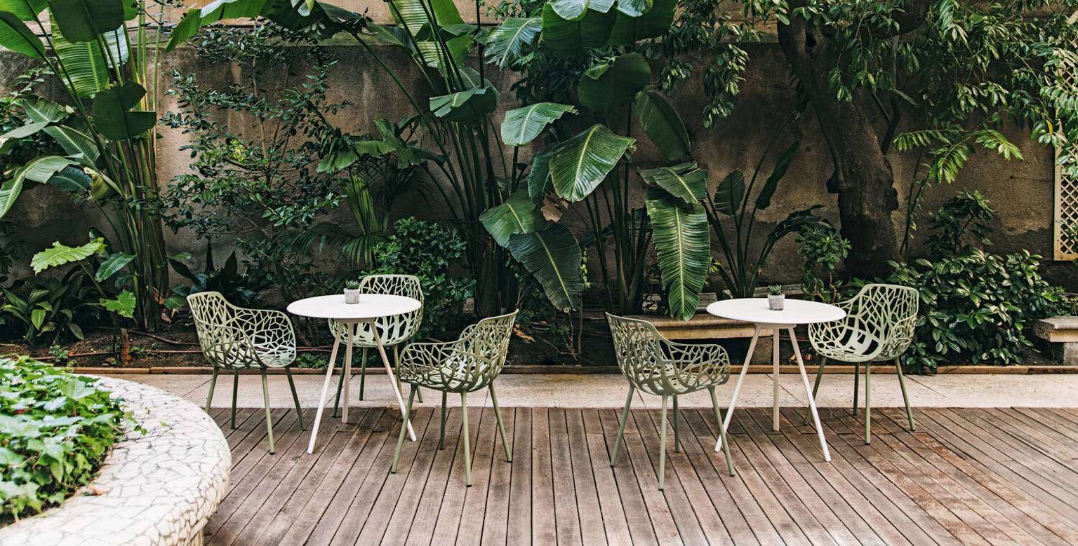 Forest chairs, with their leaf-pattern backs, around small tables on a deck among palms