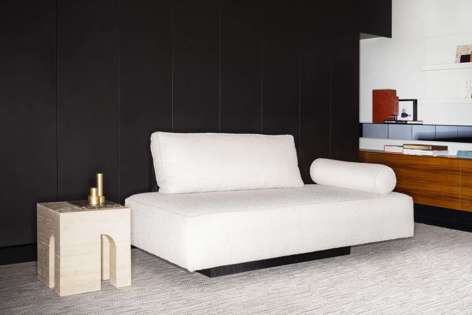 White daybed sofa against a black wall, with a stone side table