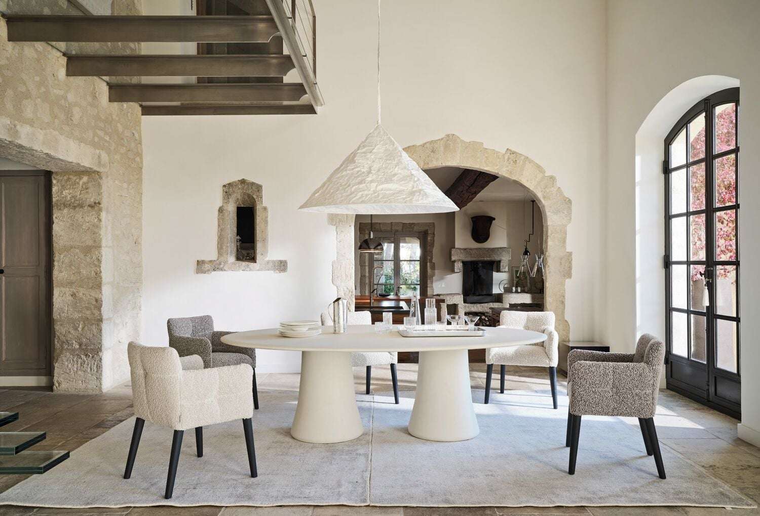 Round white dining table and upholstered chairs under a conical pendant in a stone house