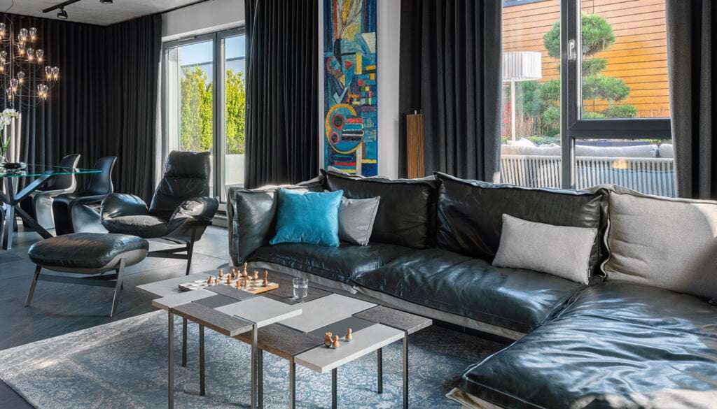 Black leather corner sofa and a lounge chair in a living room with a wall of windows