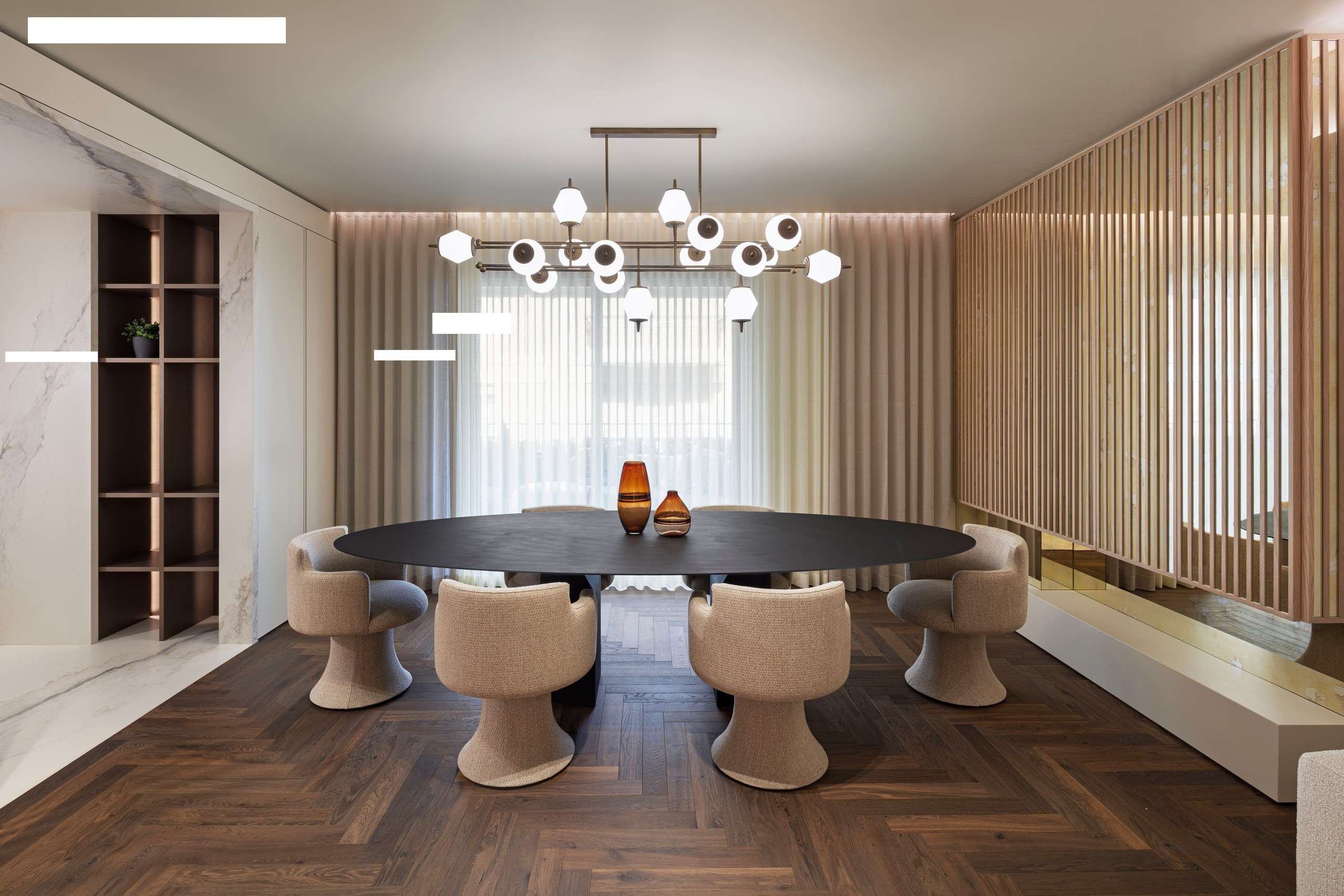Oval dining table under a glass chandelier, with slatted timber screens behind