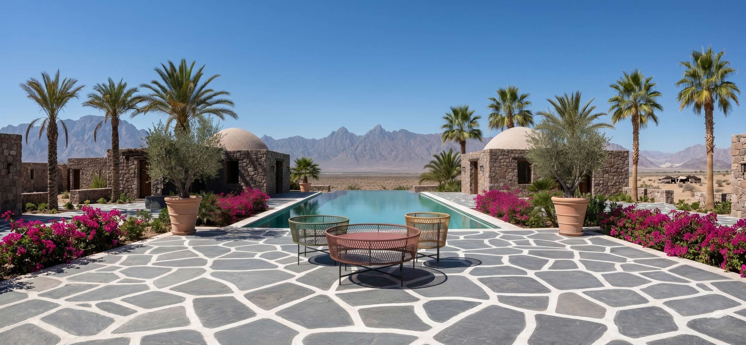 Woven outdoor chairs beside a pool on a stone terrace among palms