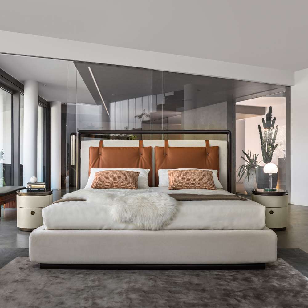 Bed with a cognac leather headboard and cream bedding between two round bedside tables