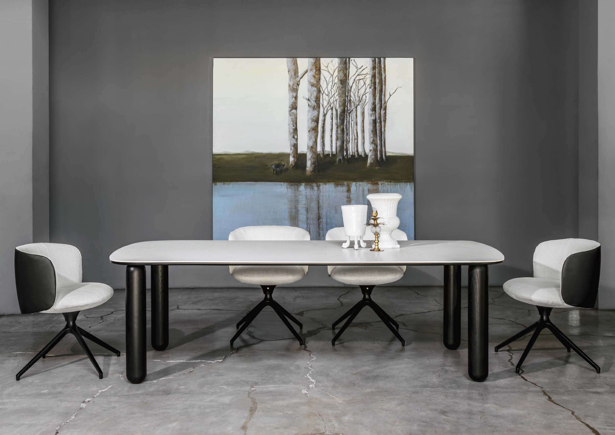 White dining table on black legs with swivel chairs before a painting of birch trees
