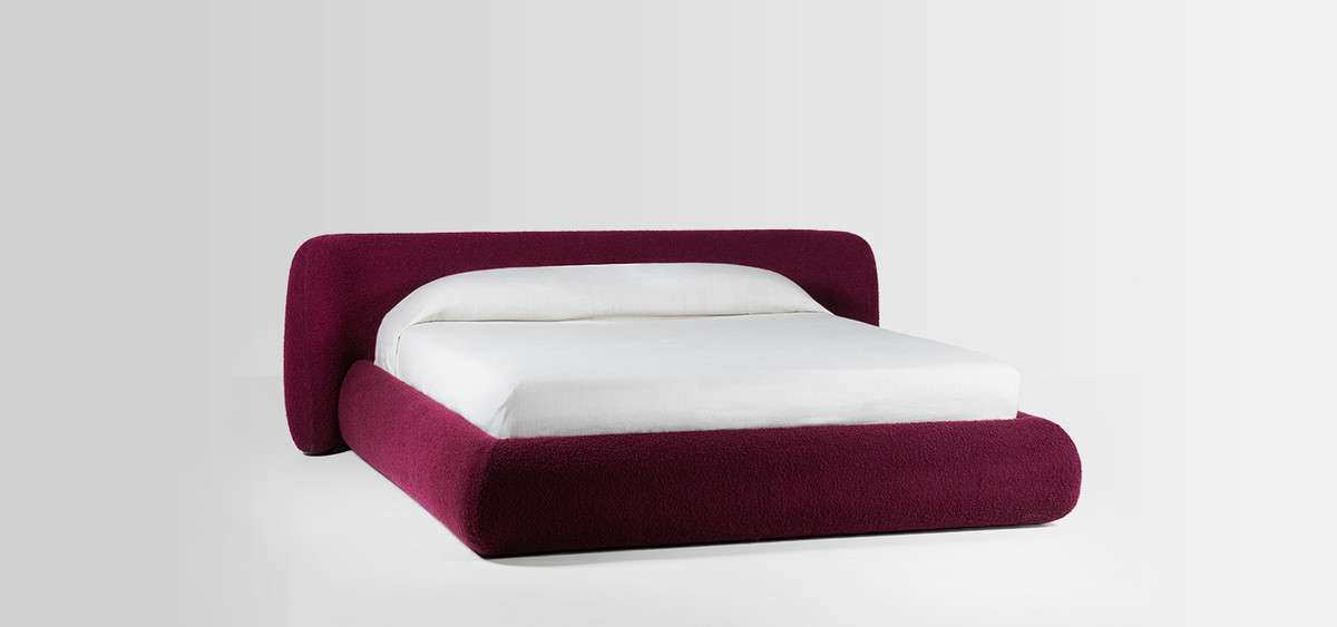 Bed with a rounded burgundy upholstered frame and white bedding