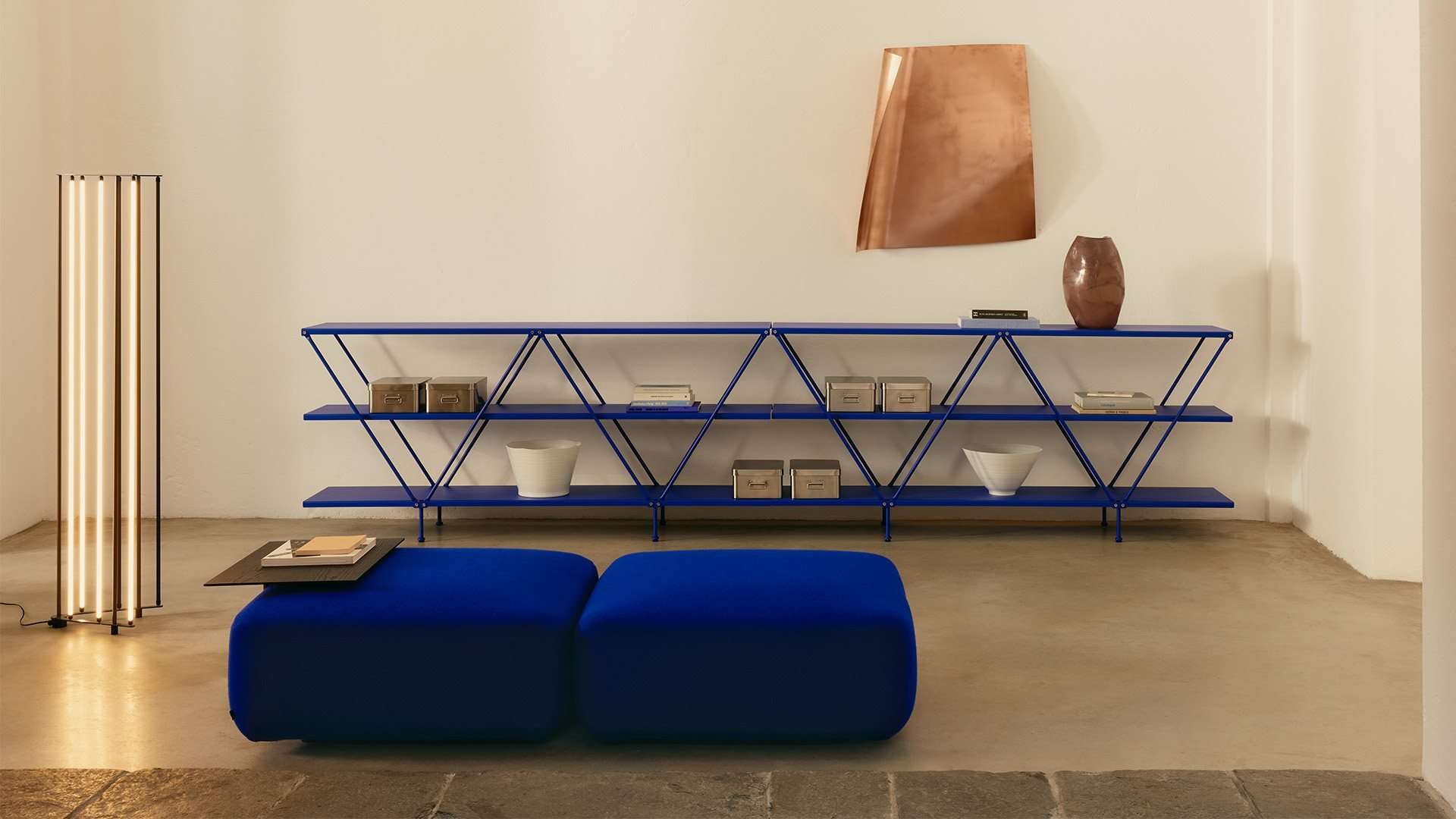 Blue wireframe shelving above a pair of blue velvet ottomans