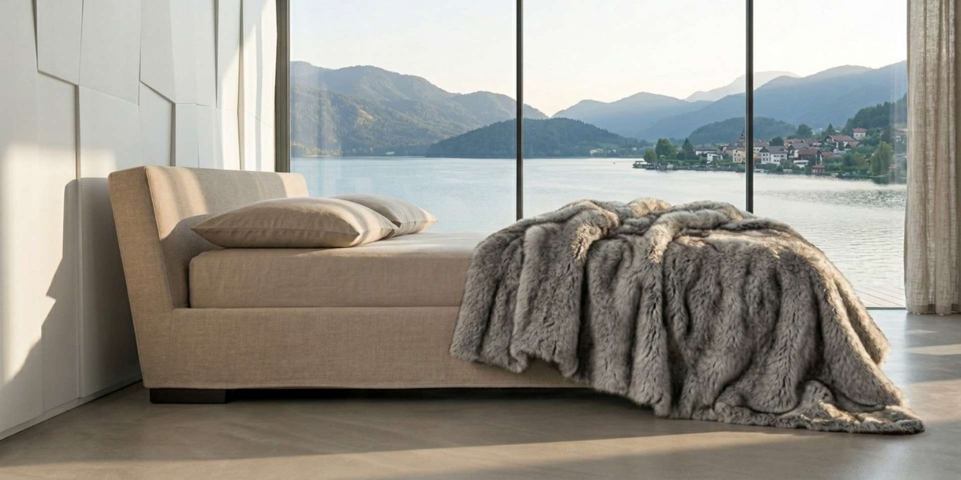 Low upholstered bed with a fur throw before a window onto a lake and mountains