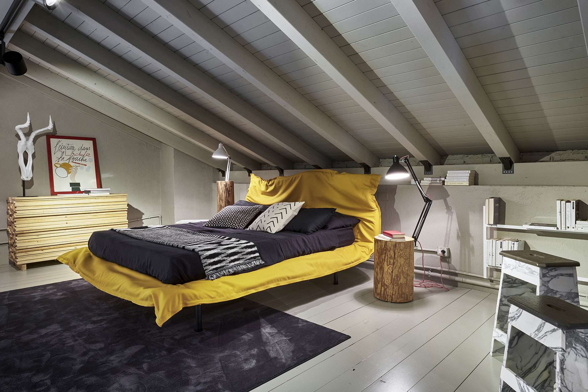 Bed with a yellow throw under white timber roof beams