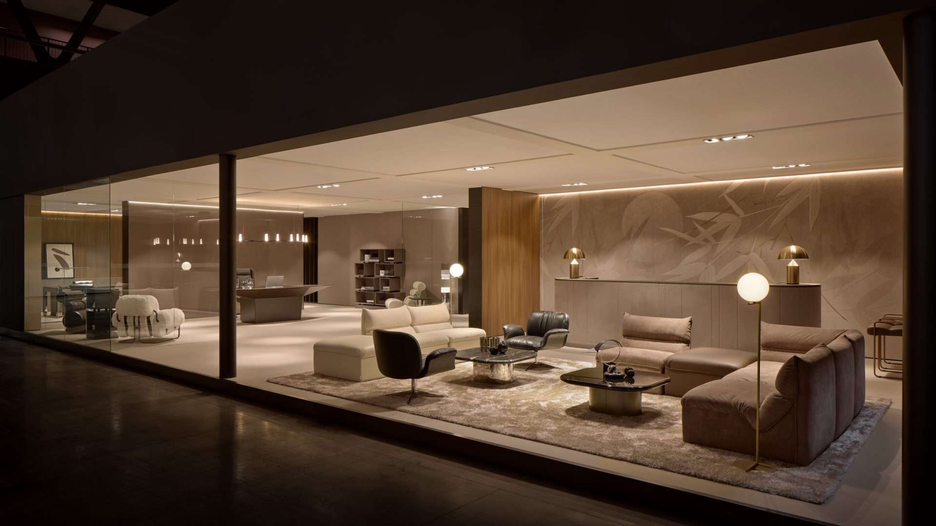 Showroom lounge with sofas and armchairs behind a long glass wall at night