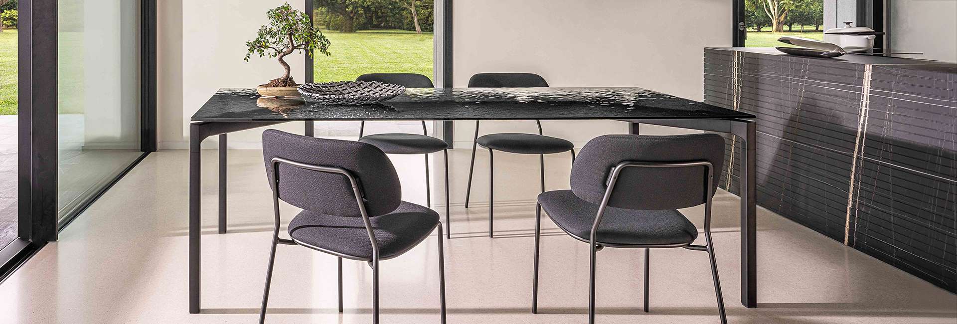 Upholstered grey chairs at a glass-topped table beside a window