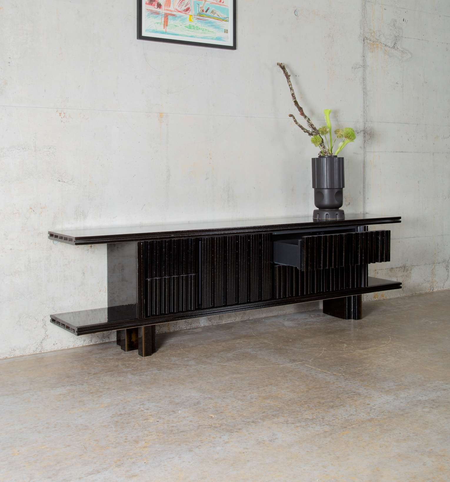 Long dark sideboard with a vase of branches against a concrete wall