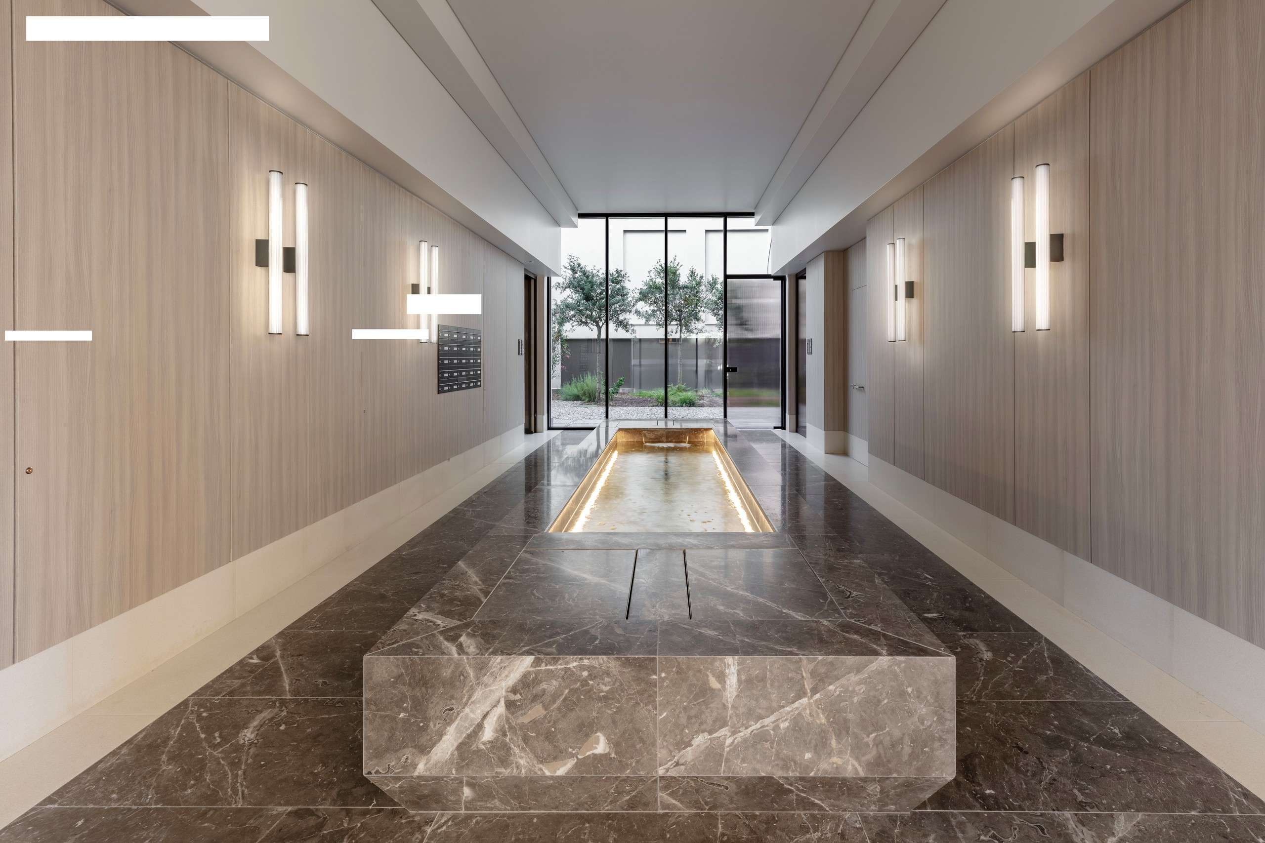 Long entrance hall with a marble bench, wall lights and a garden at the far end